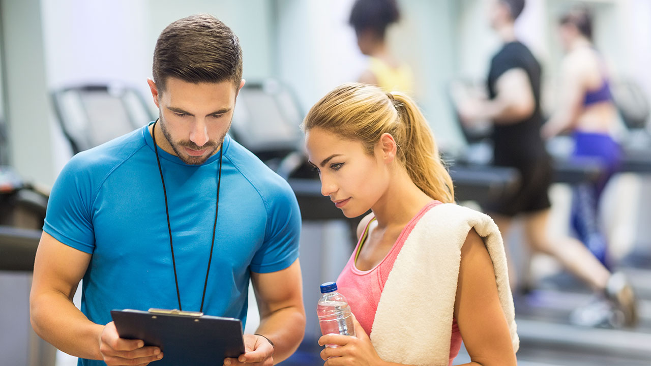 personal trainer talking to woman with clipboard at gym